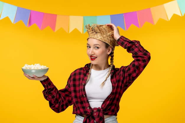 Free photo festa junina blonde cute girl in straw hat brazilian festival colorful flags holding bowl popcorn