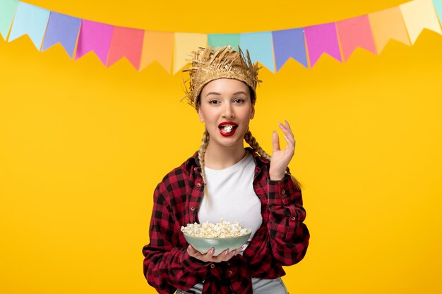 Festa junina blonde cute girl in straw hat brazilian festival with colorful flags eating popcorn