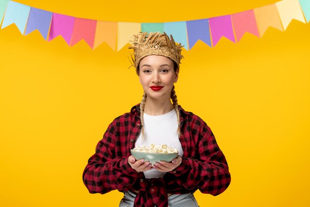 Festa junina блондинка милая девушка в соломенной шляпе бразильский фестиваль с красочными флагами, держа попкорн
