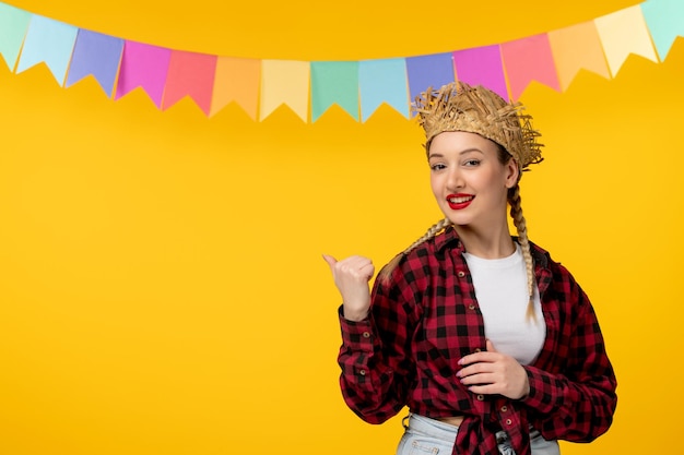 Festa junina blonde cute girl in straw hat brazilian festival with colorful flags pointing to back