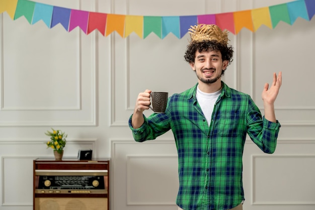 Festa junina ragazzo carino con cappello di paglia con radio retrò e bandiere colorate che tengono una tazza di caffè