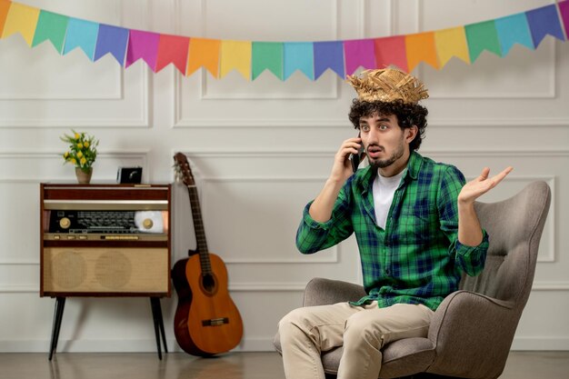 Festa junina cute young guy in straw hat with retro radio and colorful flags making phone call