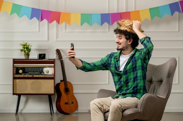 Festa junina cute young guy in straw hat with retro radio and colorful flags taking selfie