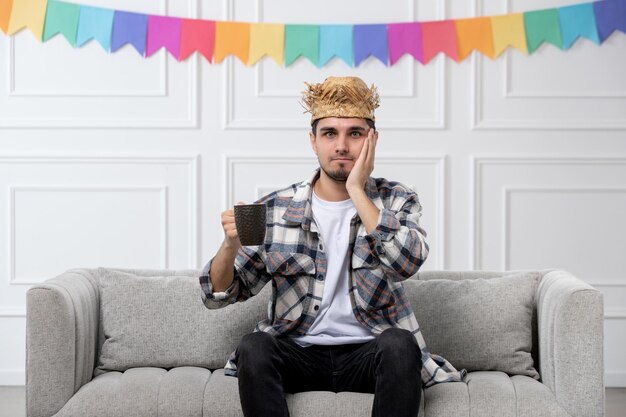 Festa junina handsome guy in checked shirt in straw hat celebrating festival confused