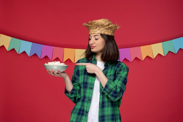 ポップコーンを食べるブラジルのお祭りを祝う麦わら帽子ブルネットのかわいい女の子のフェスタジュニーナ