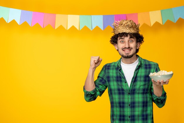 Festa junina молодой симпатичный парень в соломенной шляпе и разноцветных флагах бразильского фестиваля взволнован