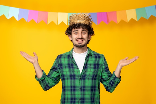 Festa junina молодой симпатичный парень в соломенной шляпе и разноцветных флагах бразильского фестиваля машет руками