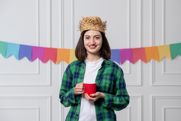 Festa junina 커피 컵을 들고 브라질 파티를 축하하는 밀짚 모자를 쓴 젊은 예쁜 소녀