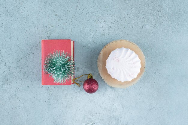 Festive arrangement of a bauble, a tree figurine on a small book and stacked cookies on marble.