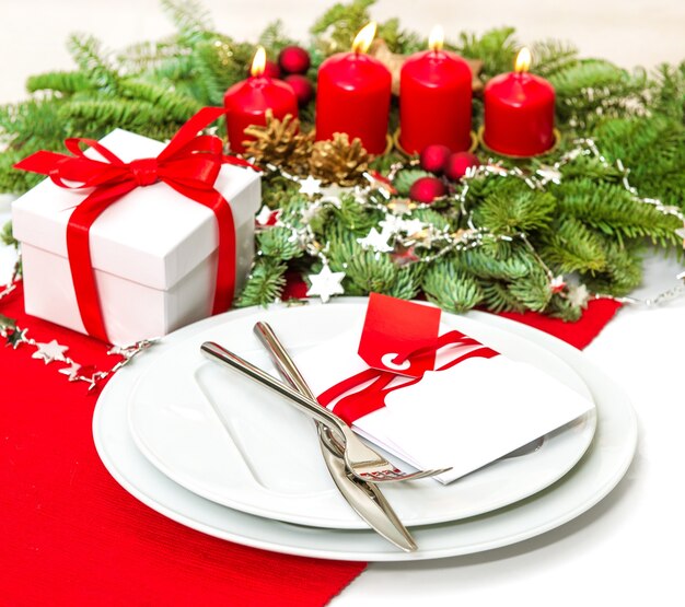 赤​で​装飾​を​設定する​お祝い​の​クリスマス​テーブル​の​場所​。 4​本​の​キャンドル​で​クリスマスツリー​の​枝​が​出現します​。​セレクティブフォーカス