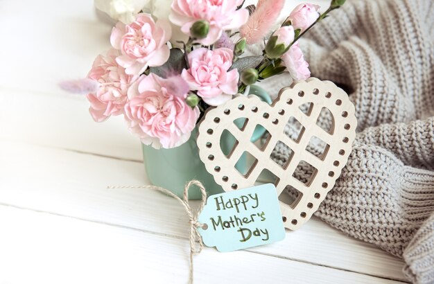 Праздничная композиция с живыми цветами в вазе, элементами декора и пожеланием счастливого Дня матери на открытке.