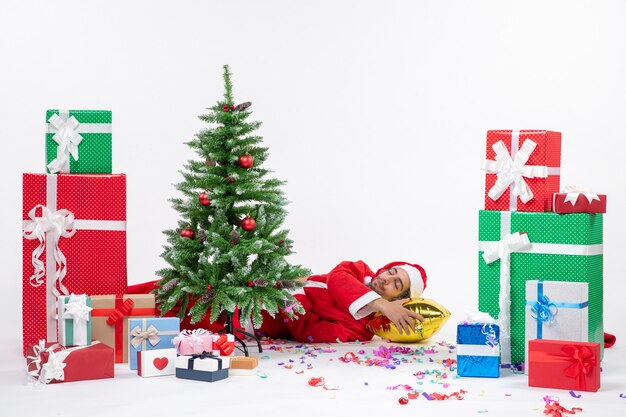 Festive holiday mood with leepings santa claus lying behind christmas tree near gifts in different colors on white background stock photo