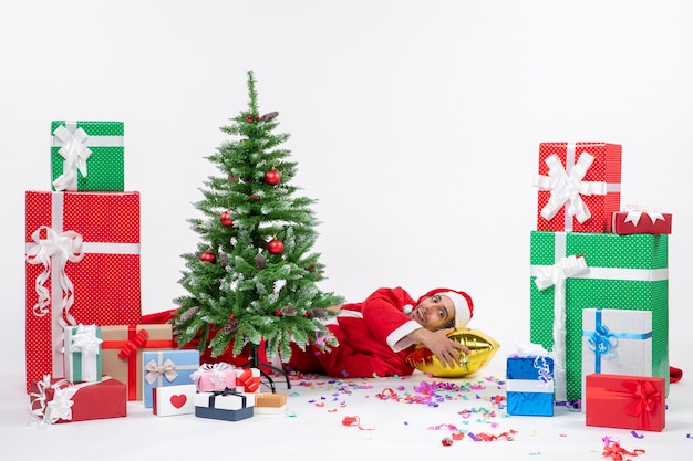 Free photo festive holiday mood with santa claus lying behind christmas tree near gifts in different colors on white background footage