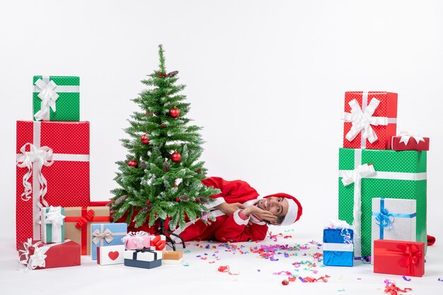 Festive holiday mood with santa claus lying behind christmas tree near gifts in different colors on white background stock photo