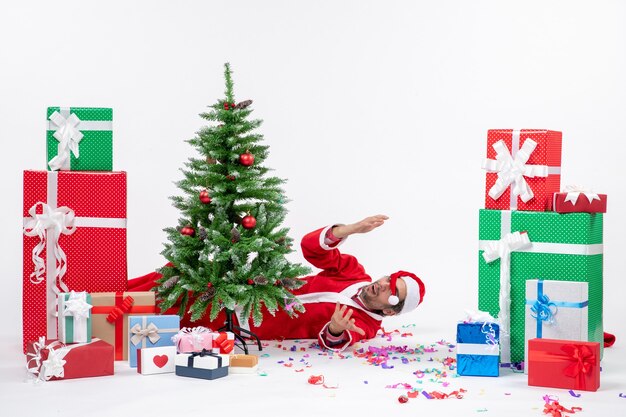 Festive holiday mood with santa claus lying behind christmas tree near gifts on white background