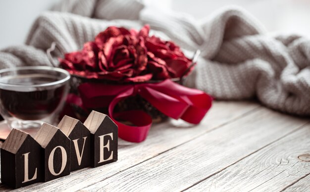 Festive home still life with wooden word love, a cup of tea and flowers on a blurred background.