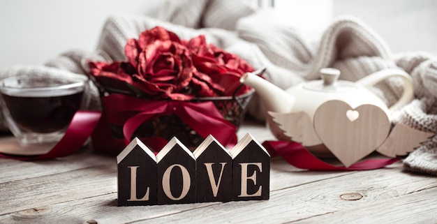 Free photo festive home still life with wooden word love, a cup of tea and a teapot on a blurred background.