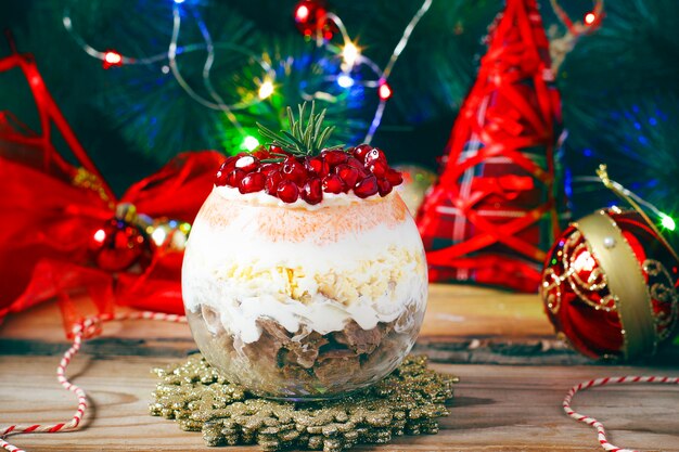 Festive layered salad serving in glass from smoked meat, egg, pomegranate seeds, carrot,  onion, mayonnaise and cheese 