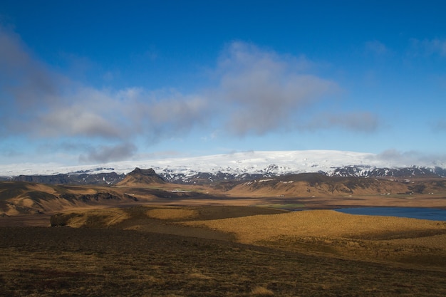 Поле в окружении воды и холмов, покрытых снегом, под облачным небом в Исландии