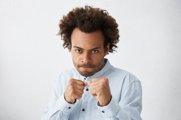 Free photo fierce and confident young dark-skinned businessman in formal wear holding fists in front of him