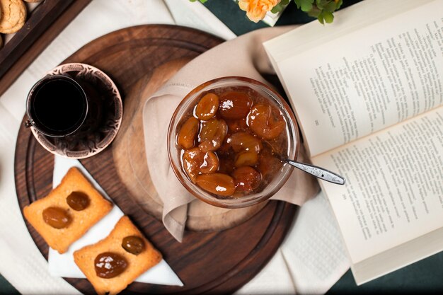 Fig confiture with a glass of black tea and some bread toasts on the wooden board.