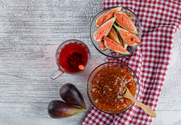 Fig jam with cup of tea, figs in a bowl on grungy and kitchen towel, top view.