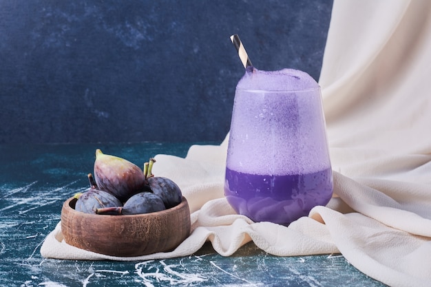 Figs in a bowl with a cup of drink on blue.