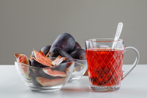 Figs in bowls with cup of tea, teaspoon side view on white and grey