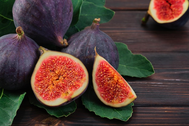 Figs and halves of several fruits closeup on the leaves of a fig tree on an old wooden table horizontal frame Seasonal fruits fig harvest background or mediterranean diet articles