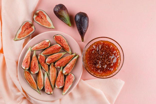 Figs with fig jam in a plate on pink and textile, flat lay.