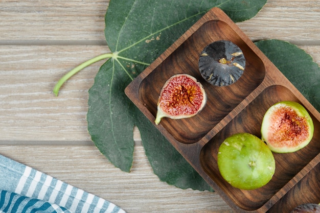 Figs in a wooden platter on the green leaves. 