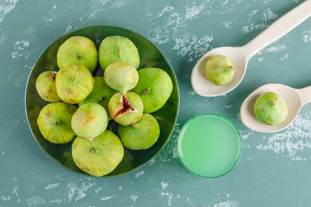 Free photo figs in wooden spoons and plate with drink flat lay on a plaster wall