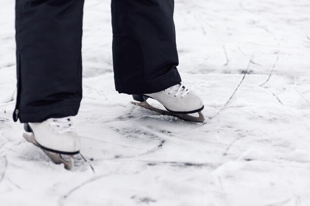 Figure skating skates closeup of mans legs in black winter pants standing on ice of frozen lake in w...