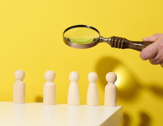 Figurines of men on a white table and magnifying glass. concept of searching for employees in the company, recruiting personnel, identifying talented and strong personaliti Premium Photo