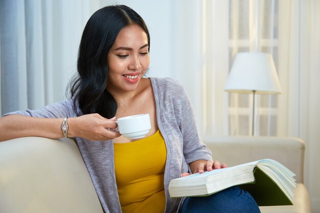 Filipino woman drinking hot beverage and reading book