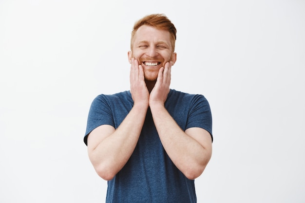 Finally beard growing. Pleased joyful happy handsome mature male with ginger hair touching bristle and smiling broadly with closed eyes, being on heaven from happiness and positive emotions