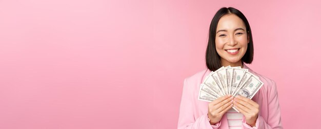 Concetto di microcredito finanziario e persone donna d'affari asiatica sorridente felice che mostra denaro in dollari in piedi in tuta su sfondo rosa