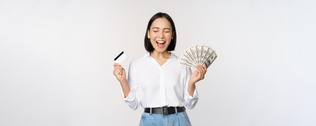 Концепция финансов и денег счастливая молодая азиатская женщина танцует с наличными и кредитной картой улыбаясь довольная