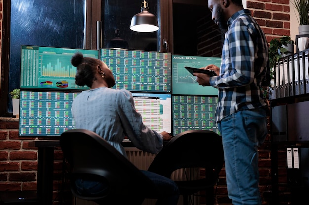 Financial analysts near multi monitor workstation using tablet device to analyze capital profit risks. Hedge fund company professional agents in office, reviewing trading strategies to take profits.