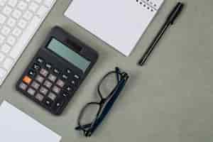 Бесплатное фото Финансовая концепция с ноутбука, бумага, ручка, калькулятор, клавиатура, очки на сером фоне плоской планировки.