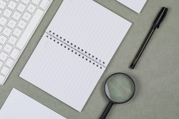 Финансовая концепция с ноутбуками, бумага, ручка, увеличительное стекло, клавиатура на сером фоне плоской планировки.