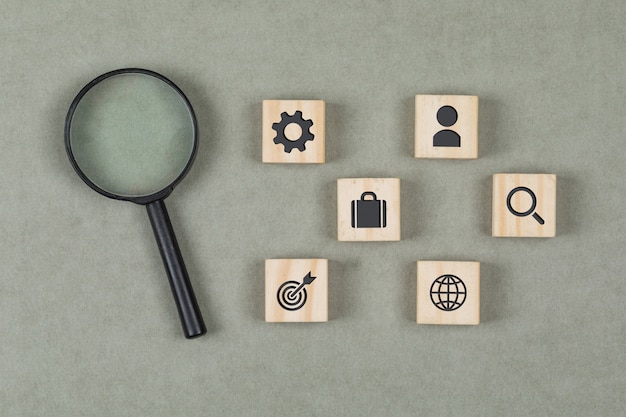 Financial concept with wooden cubes, magnifying glass on grey background flat lay.