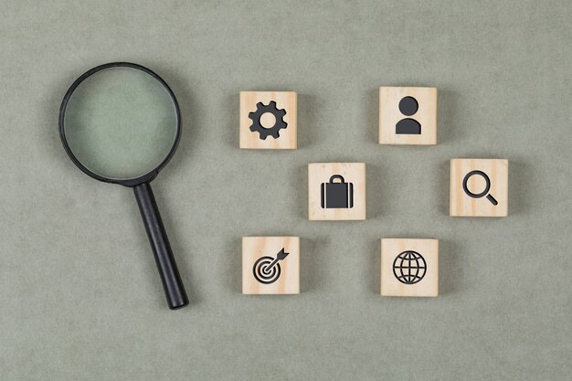 Financial concept with wooden cubes, magnifying glass on grey background flat lay.