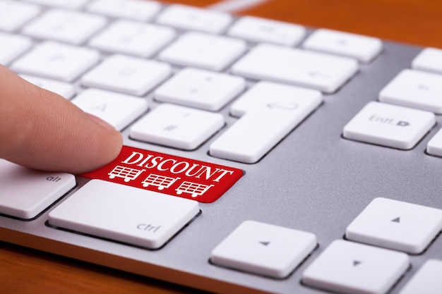 赤いキーボードの割引ボタンを指で押します。オンライン販売。指と言葉の横に3つのショッピングカートがあります