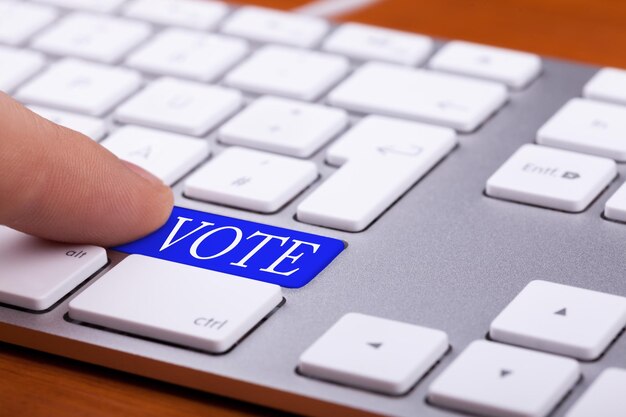 Finger pressing on vote blue button on keyboard. Online elections