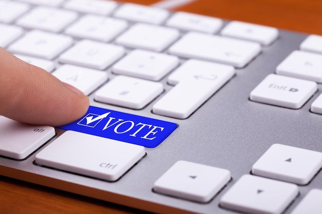 Finger pressing on vote blue button and symbol on keyboard. Online elections