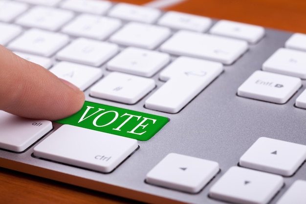 Finger pressing on vote green button on keyboard. Online elections
