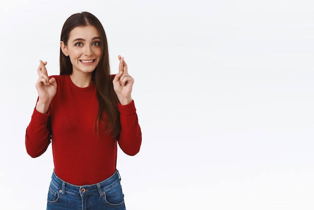 Fingers crossed for everything go well Slightly nervous cute caucasian girl in red sweater praying for dream come true looking excited and worried praying willing aspirations fulfill