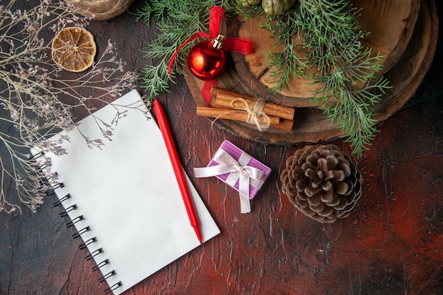 Fir branches and closed spiral notebook with pen cinnamon limes conifer cone and ball of rope on dark background above view