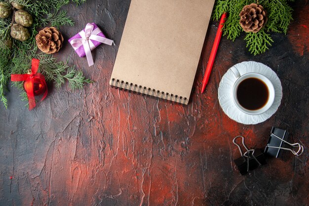 Fir branches a cup of black tea decoration accessories and gift next to notebook with pen on dark background